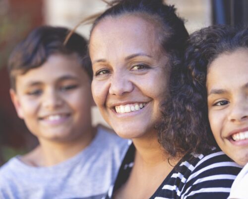Aboriginal Family portrait with 1 parent and 2 children. They are sitting on the front porch. Everyone is happy and smiling. Could be a single mother.